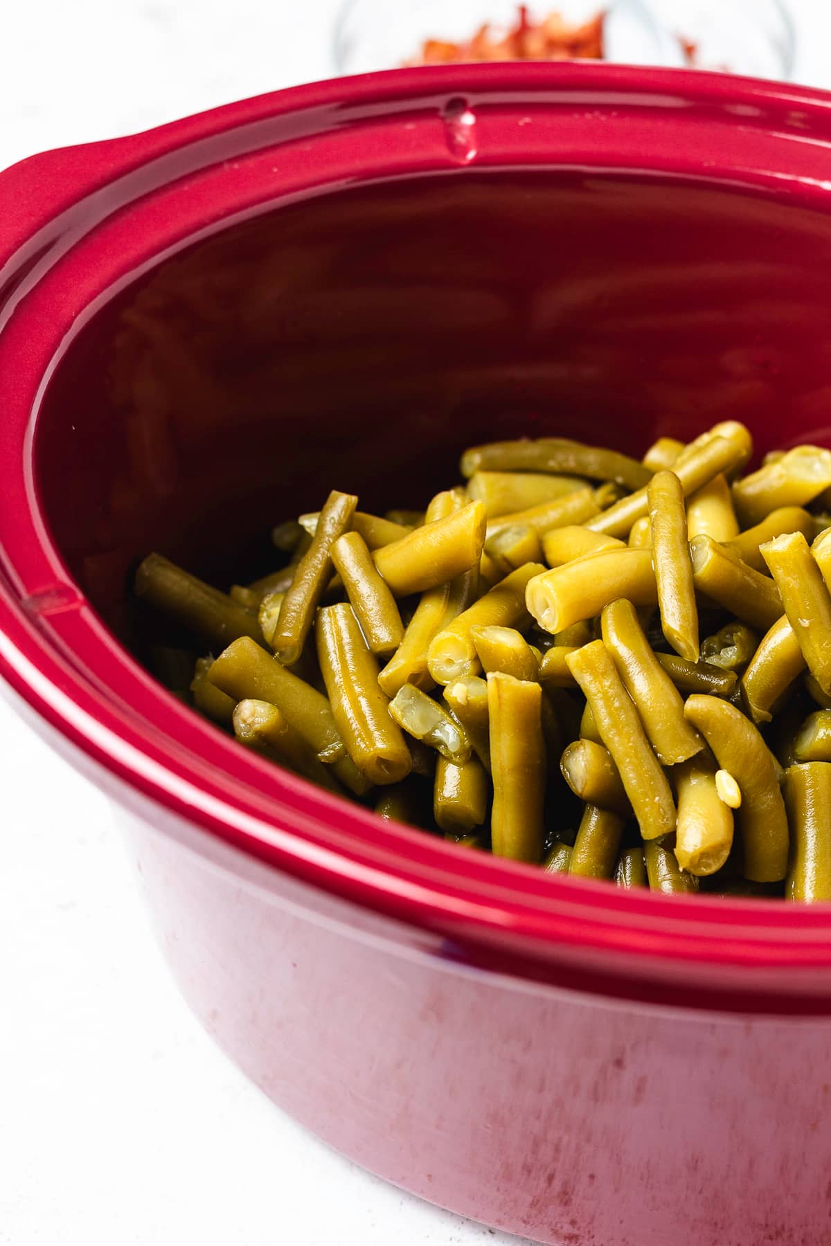 Cut green beans in a red slow cooker before adding the brown sugar glaze and bacon.