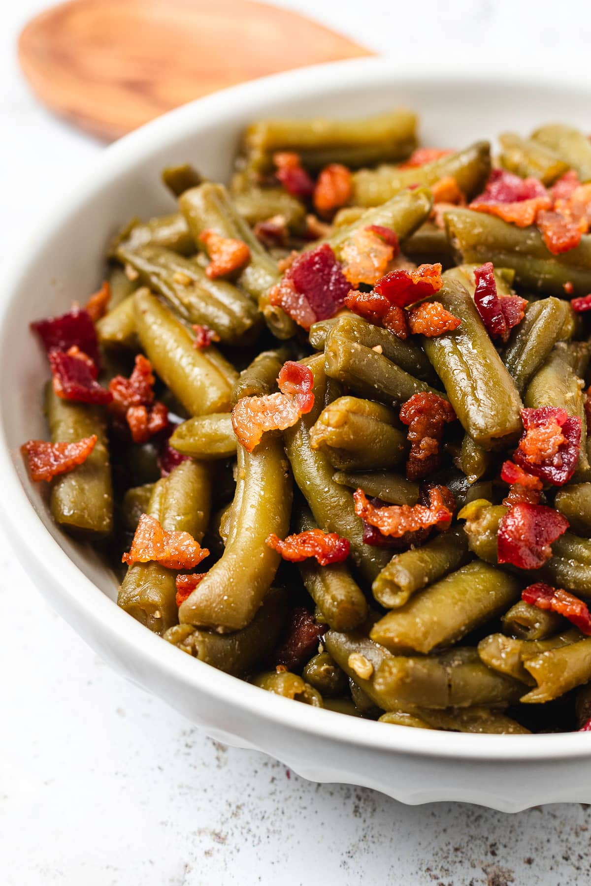 Close-up of slow cooker crack green beans coated in a savory glaze and topped with crispy bacon in a white bowl.