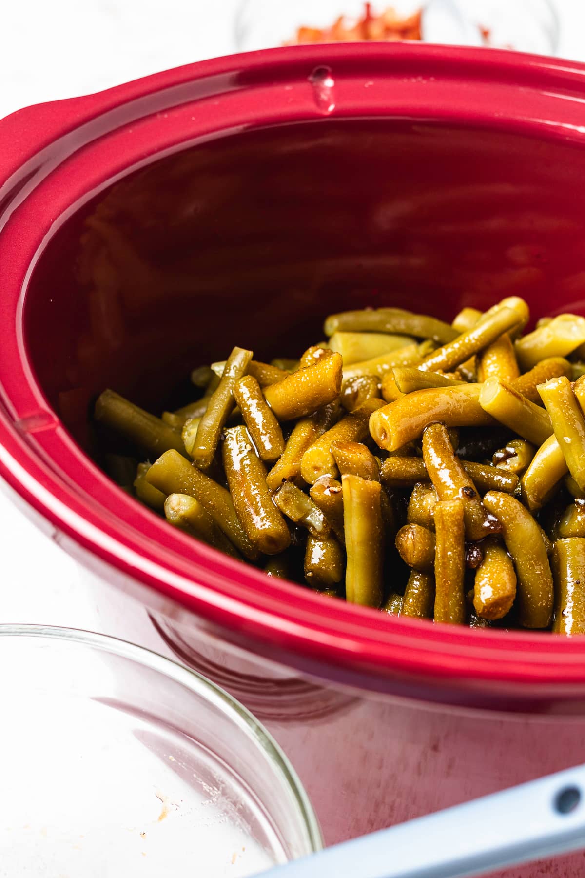Green beans coated in a glossy brown sugar sauce inside a red slow cooker.