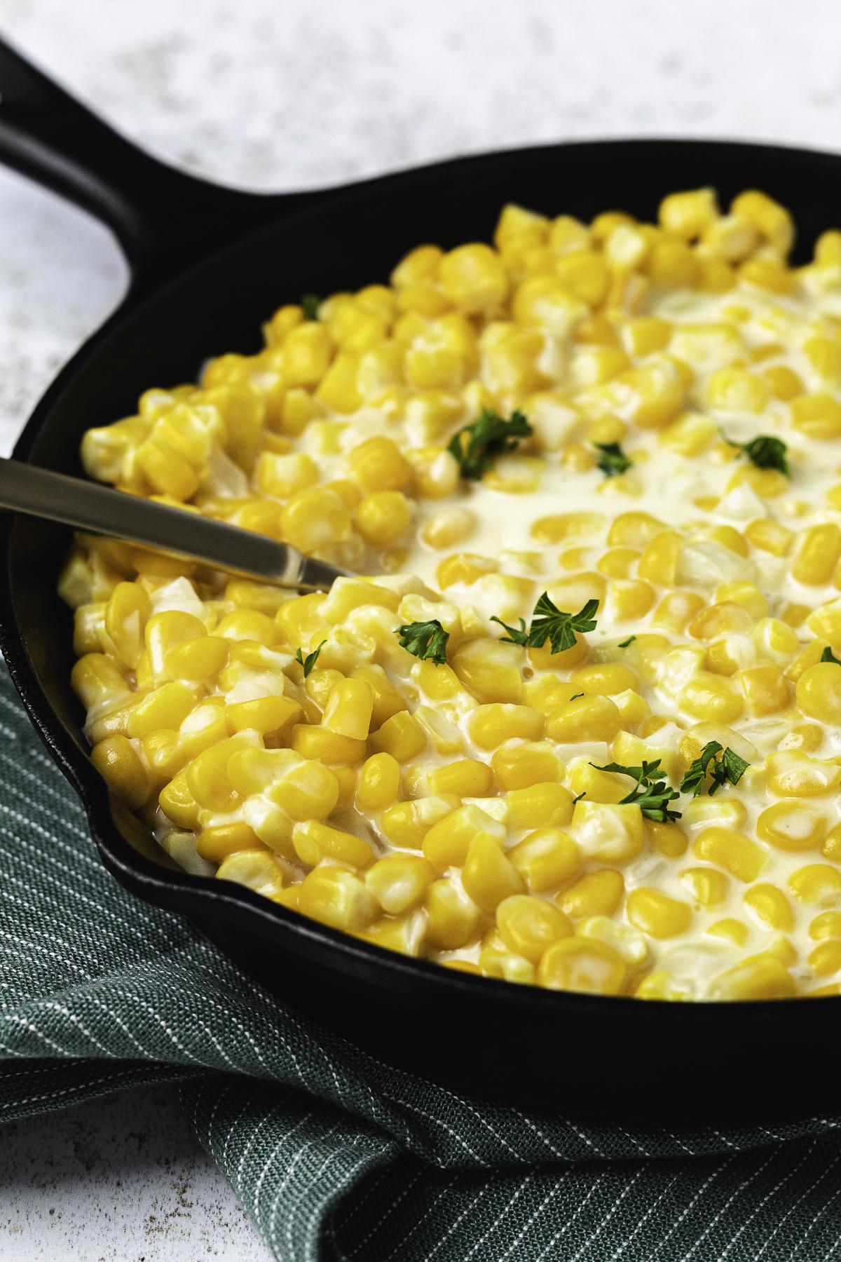 Close-up of homemade stovetop creamed corn in a black skillet with a rich cream sauce and parsley.