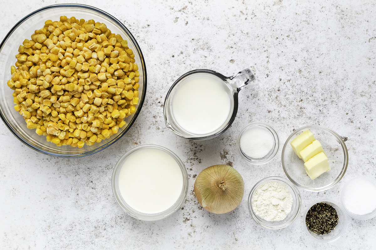 Corn, milk, cream, butter, onion, flour, sugar, salt, and pepper arranged for homemade stovetop creamed corn.