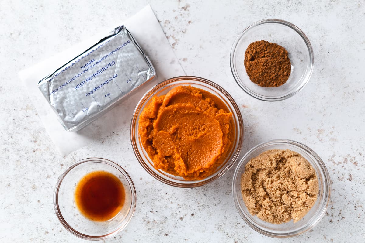Pumpkin cheesecake ingredients including cream cheese, pumpkin puree, brown sugar, vanilla, and pumpkin spice.