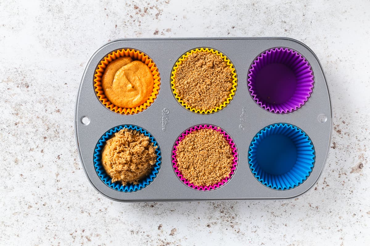 Graham cracker crumb topping added over mini pumpkin cheesecake bites in silicone liners.