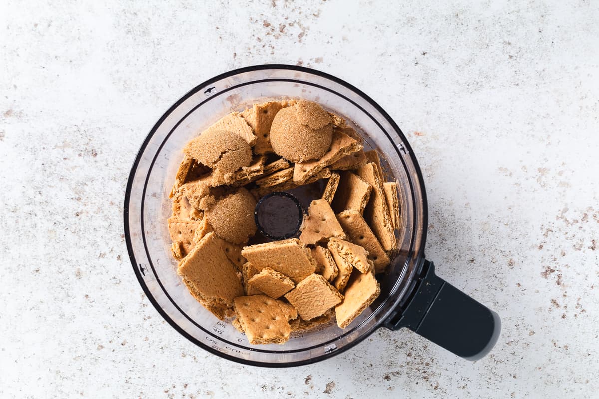 Graham cracker pieces and brown sugar added to a food processor for the cheesecake crust.