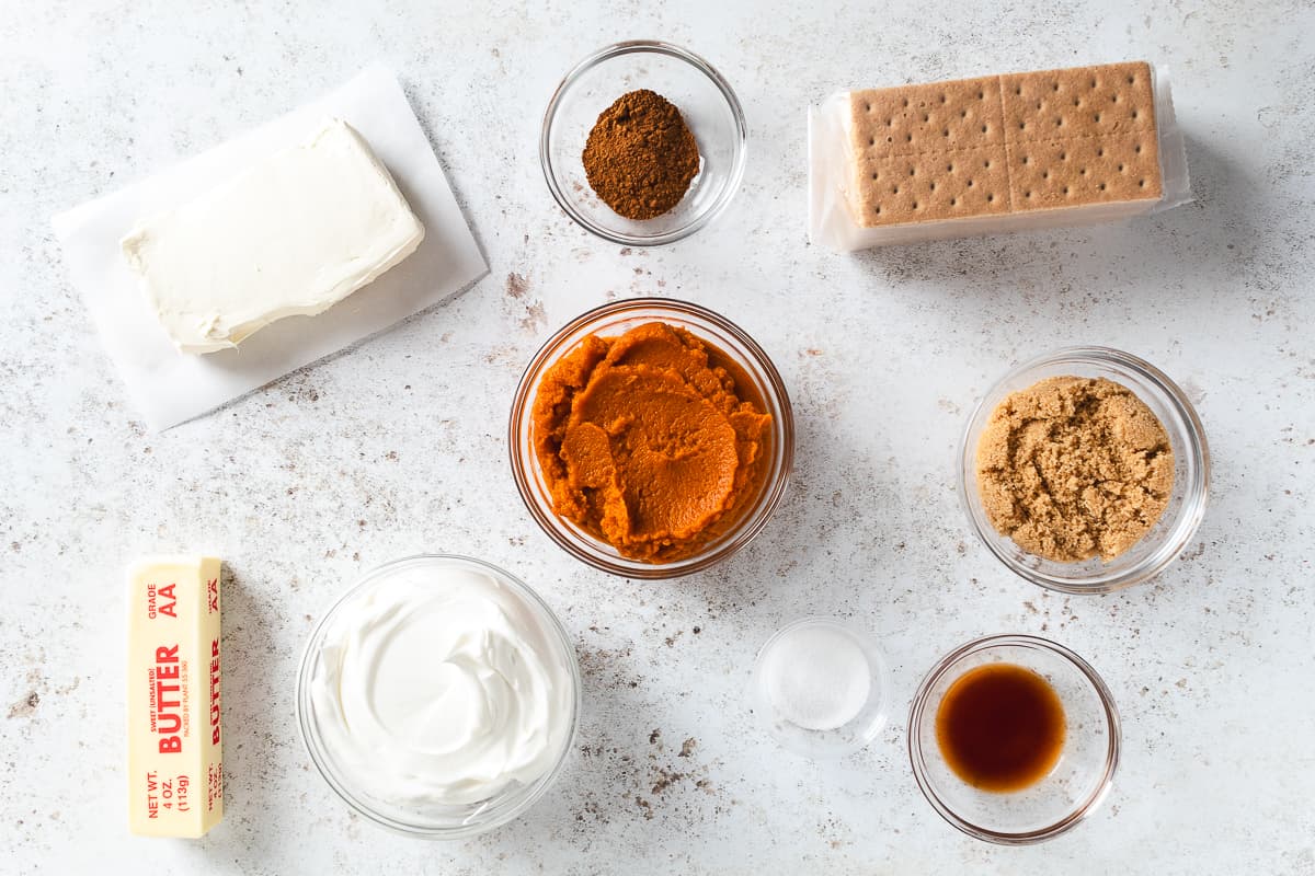 Ingredients for pumpkin spice cheesecake cups including cream cheese, pumpkin, graham crackers, butter, brown sugar, vanilla, and spices.