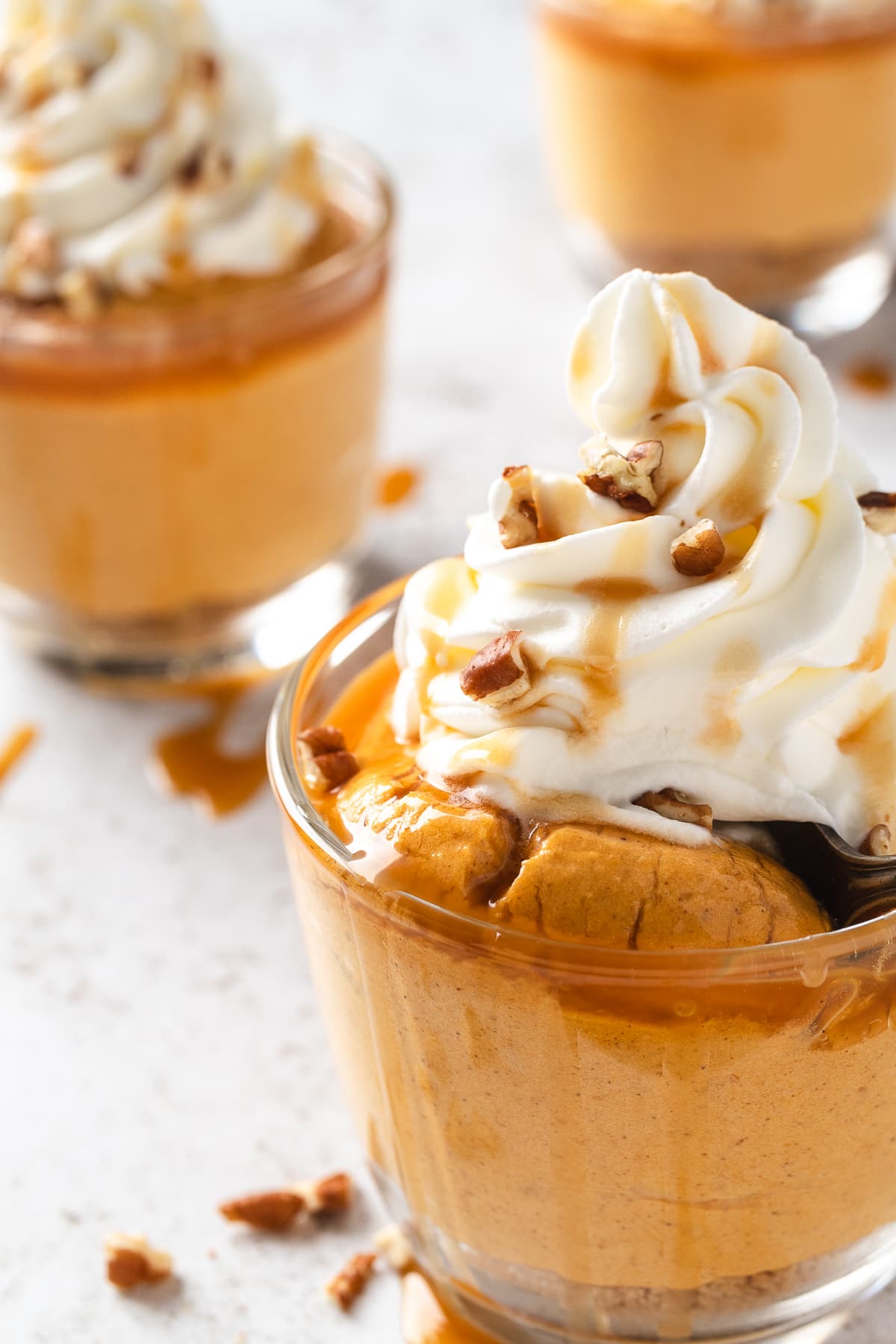 Individual pumpkin spice cheesecake cup topped with whipped cream, caramel drizzle, and chopped pecans.