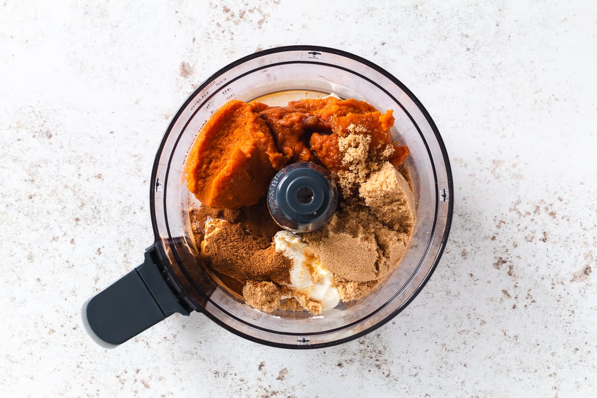 Pumpkin cheesecake ingredients added to a food processor before blending.