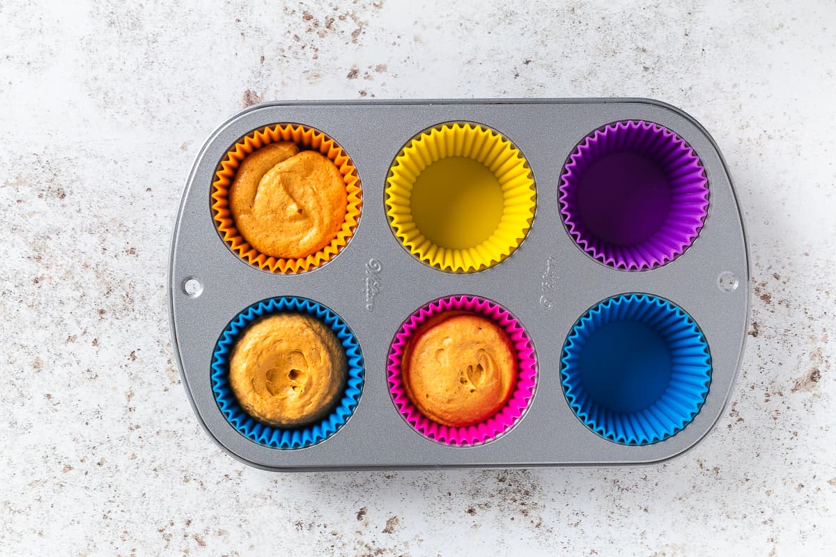 Mini pumpkin cheesecake batter portioned into colorful silicone liners in a muffin pan.